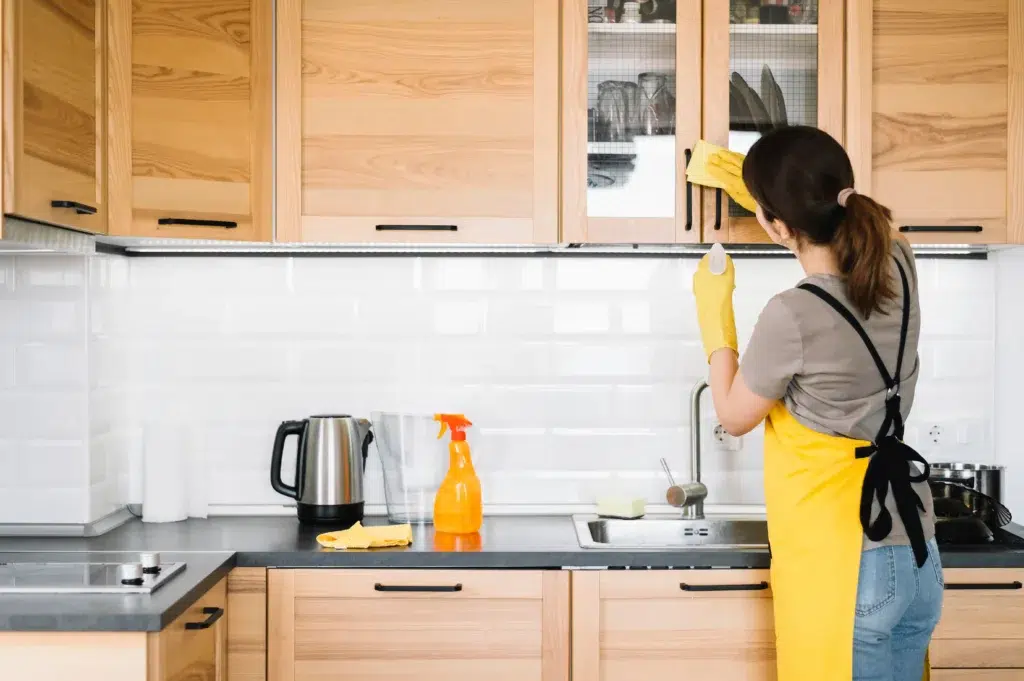 Professional cleaner wiping kitchen cabinets and surfaces during fall deep cleaning in Staten Island home